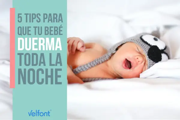 Un bebé con gorro de búho, con la boca abierta, en la cama. 5 consejos para que tu bebé duerma toda la noche.