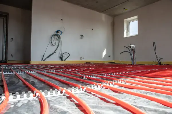 Instalacja podłogówki w garażu w trakcie budowy. Czerwone rurki systemu grzewczego ułożone na folii izolacyjnej.