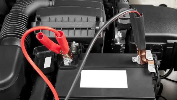Jumper cables connected to a car battery. Learn how long to leave jumper cables on for a successful jump start.