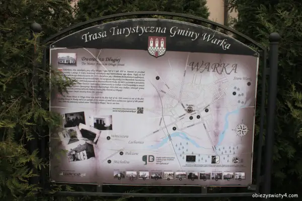 Mapa turystyczna gminy Warka z zaznaczonymi zabytkami, w tym Dworkiem na Długiej. W tle drzewa, a na dole strony logo "Warka" i adres strony.