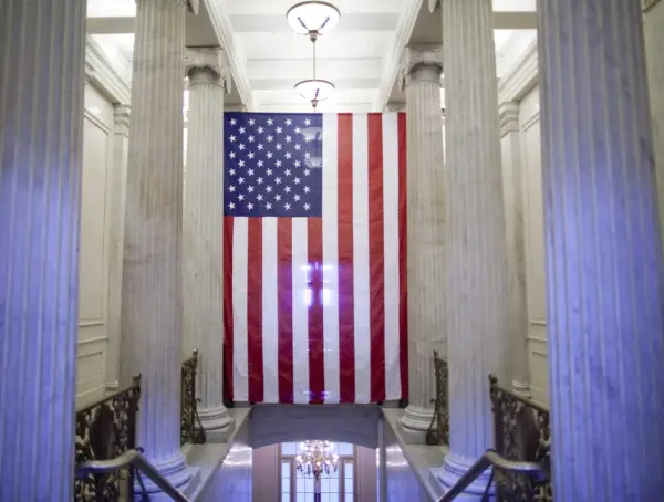 Wielka flaga USA wisi między marmurowymi kolumnami. Czy USA to stany zjednoczone? Tak, to symbol tego kraju.