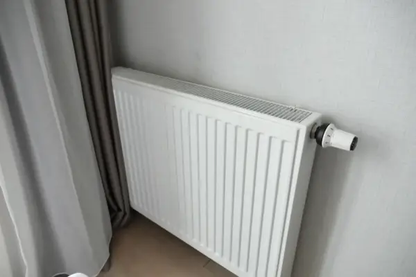 Biały grzejnik panelowy z termostatem, idealny do pokoju 16m2. Obok zasłony.