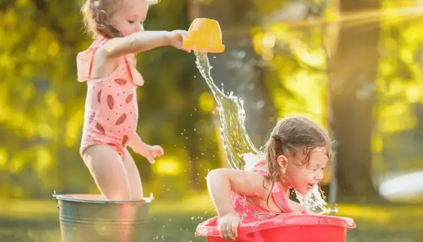 Bambine felici si divertono con giochi d'acqua sotto il sole estivo, spruzzandosi a vicenda con secchielli e bacinelle.