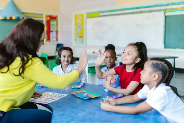 Une enseignante donne une tape dans la main à des enfants autour d'une table dans une salle de classe.