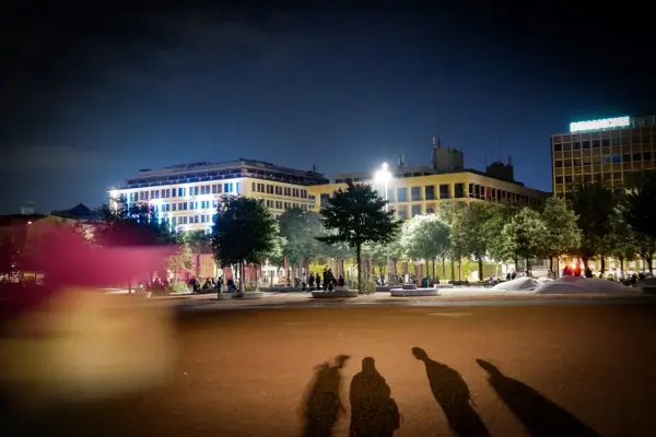 Ombre d'un mineur dehors la nuit, projetées sur une place éclairée par des bâtiments modernes.