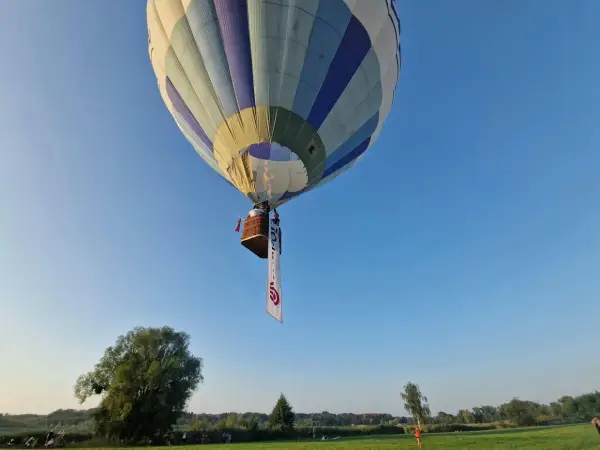 Balon z koszem i banerem unosi się na błękitnym niebie. Może to symbolizować wolność, jak w piosence "99 luftballons znaczenie".