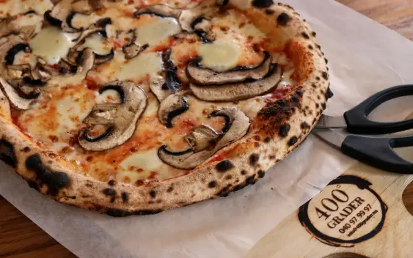 En nybakad champinjonpizza med bubblande ost, redo att skäras med saxen. En perfekt pizza för alla som gillar 400grader recensioner.