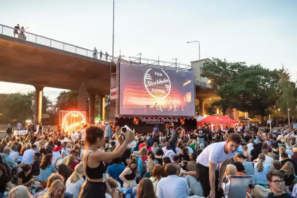 Stor publik samlad för utomhusbio under Stockholms Filmfestival. En stor duk visar festivalens logotyp.