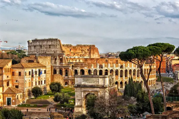 Colosseo e Arco di Tito, un'idea di cosa vedere a Roma in un giorno gratis, con pini romani e cielo nuvoloso.