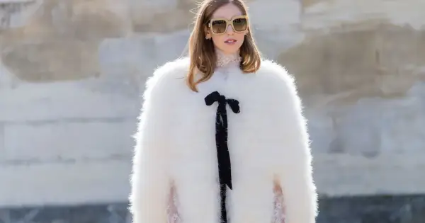 Estilo maximalismo: mujer con abrigo blanco de pelo, gafas grandes y lazo negro.