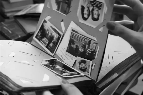 Odkryj, jak zrobić fotoksiążkę, przeglądając stare zdjęcia w albumie. Ręka trzyma kartę z portretami i krajobrazami.