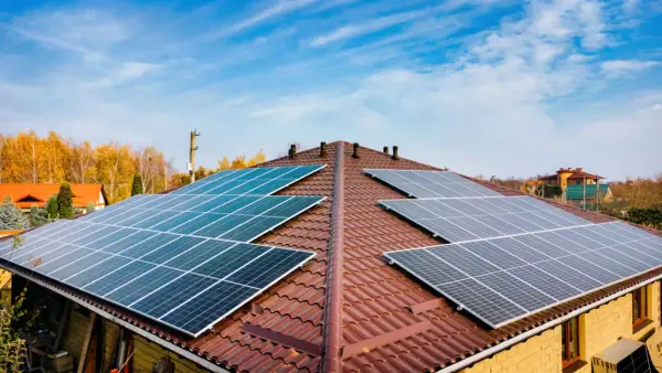Dach pokryty brązową dachówką z zainstalowanymi panelami fotowoltaicznymi. Widać kilka rzędów ogniw monokrystalicznych, które zbierają energię słoneczną.