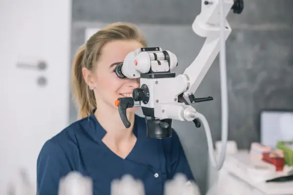 Dentystka wykonuje leczenie kanałowe pod mikroskopem, precyzyjnie pracując z użyciem nowoczesnego sprzętu.