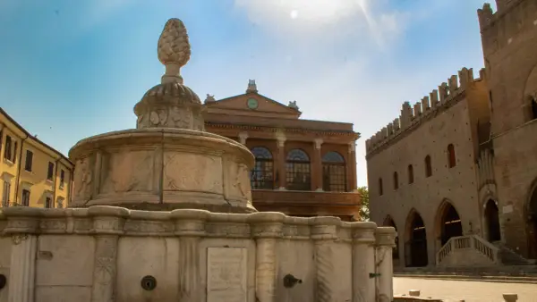 Fontana in pietra con pigna, edifici storici e cielo azzurro. Un assaggio dei monumenti di Rimini.