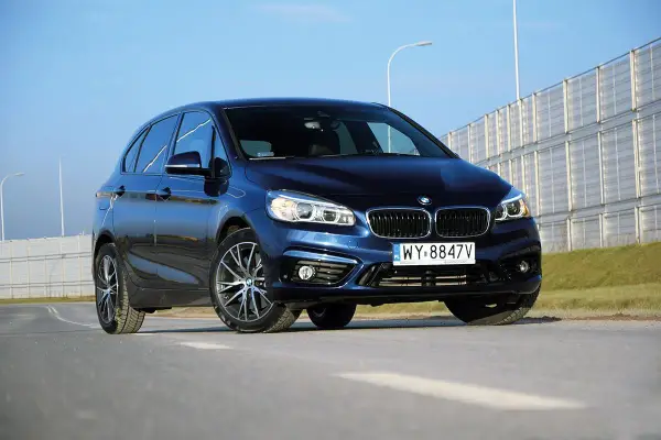 Ciemnoniebieski BMW van na tle jasnego nieba i barier dźwiękochłonnych.
