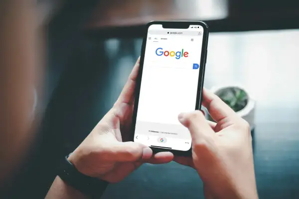 Ręce trzymające smartfon z otwartą wyszukiwarką Google. Szukasz informacji, jak usunąć konto Google z telefonu po resecie?