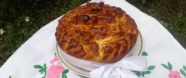 Obrzędowe ciasto weselne, bogato zdobione, z plecionkami i kwiatami z ciasta, na haftowanym obrusie.