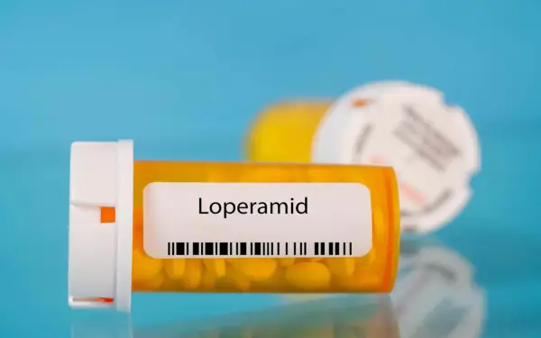 Orange pill bottle with "Loperamid" label and yellow pills inside. Another blurred bottle in the background.