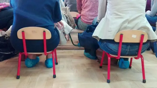 Dostateczny, jaka to ocena? Dzieci siedzą na małych krzesełkach w niebieskich ochraniaczach na buty.