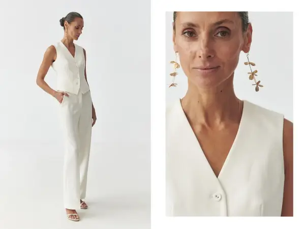 Elegancka kobieta prezentuje, jak nosić kamizelkę damską w stylizacji z białymi spodniami. Długie kolczyki dodają szyku.