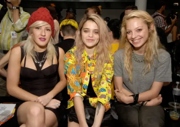 Tres jóvenes con un estilo que evoca el "heroin chic" posan juntas. Una lleva un gorro rojo, otra una chaqueta colorida y la tercera una camiseta gris.
