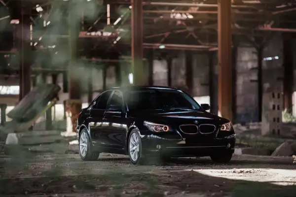 Czarny BMW 535d w opuszczonej hali, otoczony mgłą i gruzem.