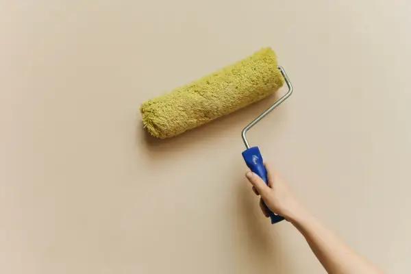 En hand håller en färgroller med gul päls, redo att måla en vägg. Kanske är det dags för en 3m rubbing för att fräscha upp hemmet.