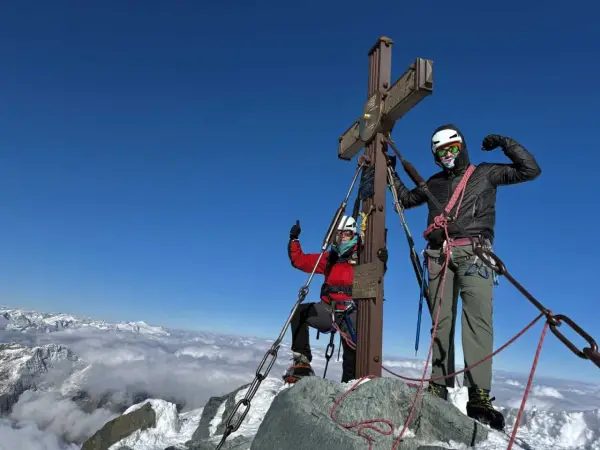 Dwóch alpinistów na szczycie najwyższego szczytu w Austrii. Widok na góry i chmury poniżej.