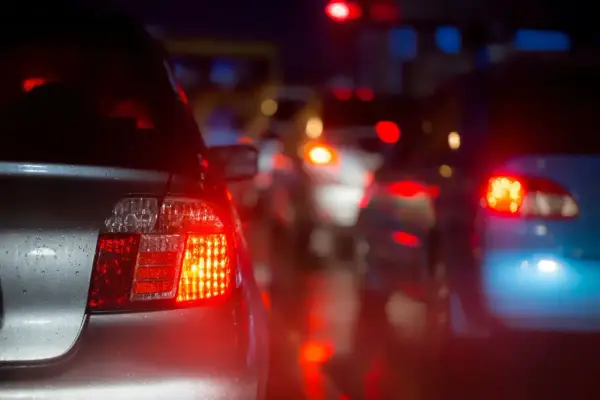 Czerwone światła stopu, czyli "brems licht co to znaczy", oznaczają hamowanie. Samochody stoją w korku nocą, ich światła odbijają się na mokrej drodze.