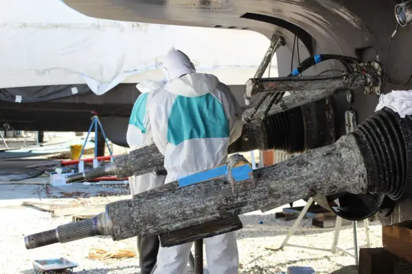 Travailleurs en combinaison protègent un bateau aluminium contre l'électrolyse. Des pièces rouillées sont visibles.