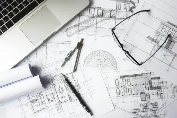 Na stole leżą plany architektoniczne, laptop, cyrkiel, linijka i okulary. To idealne miejsce do pracy nad kosztorysem budowlanym wzór.