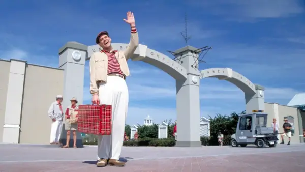 Truman Show obsada: Jim Carrey wita się z widzami, trzymając czerwoną walizkę. W tle łuk z napisem "Omnibus".