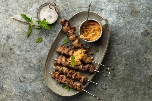 Brochettes d'agneau grillées au barbecue, servies avec une sauce aux arachides et garnies de menthe fraîche.