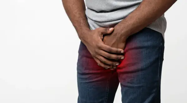 Mężczyzna trzyma się za krocze, gdzie widoczny jest czerwony obszar bólu, sugerujący ropień prostaty.