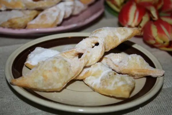 Chrupiące faworki, przepis babci, posypane cukrem pudrem, na talerzu obok tulipanów.