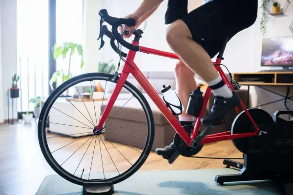 Intensywny trening na trenażerze kolarskim w domu. Czerwony rower, sportowiec w spodenkach i koszulce, butelki z wodą.