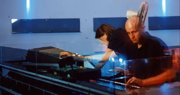 Robert Henke und Kollegin im Studio, umgeben von blauem Licht und Musik-Equipment.