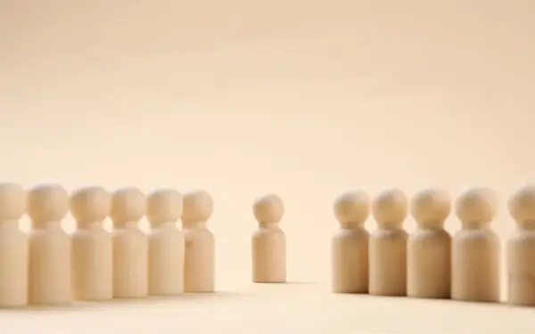 Un pupazzetto di legno si erge da solo, separato da un gruppo. Un simbolo di imparare a stare da soli, trovando forza nella propria individualità.
