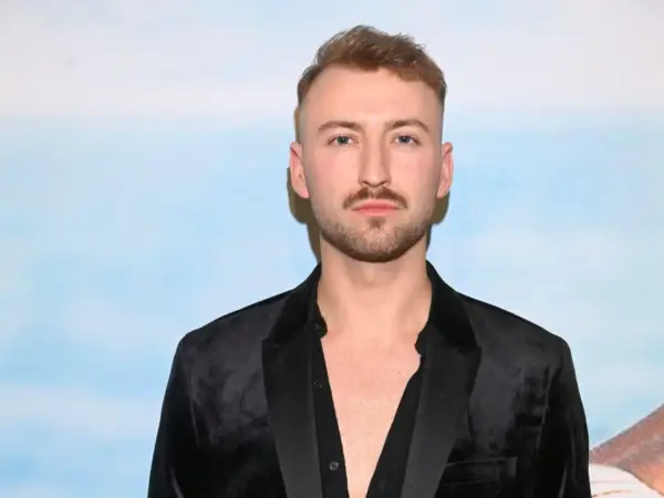 Michał Bartkiewicz w czarnym aksamitnym marynarkowym stroju, z zarostem i fryzurą, na tle błękitnego nieba. Jego życie prywatne budzi zainteresowanie.