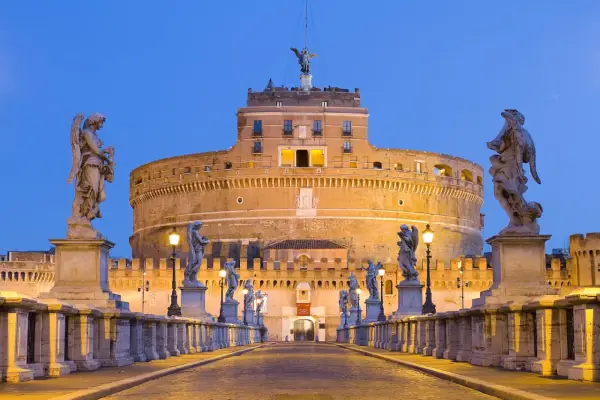 Ponte Sant'Angelo illuminato di sera, con le statue degli angeli e Castel Sant'Angelo sullo sfondo. Curiosità: la statua in cima al castello.