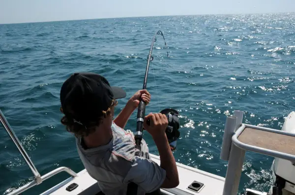 Ragazzo con cappellino nero pesca in mare, mostrando alcuni metodi di pesca con la canna.