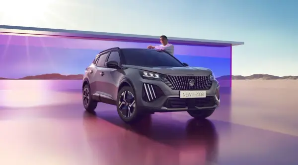Mężczyzna opiera się o maskę nowego Peugeot E-2008, stylowego peugeot suv, na tle futurystycznej architektury i pustynnego krajobrazu.