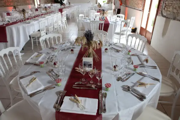 Une table dressée à la française, prête pour un événement. Nappes blanches, chemins de table bordeaux, vaisselle et couverts élégants, et une touche champêtre avec des épis de blé et de la lavande.
