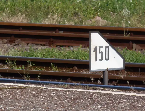 Biały trójkątny wskaźnik w11 z czarną liczbą 150 obok torów kolejowych.