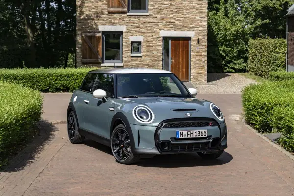 Nowoczesny Mini Cooper w kolorze miętowym stoi przed kamiennym domem. Zastanawiasz się, ile pali ten model?