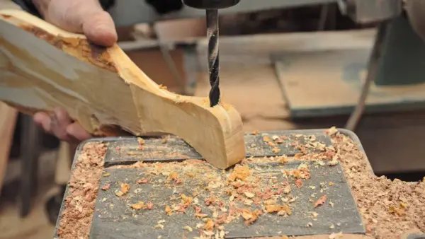 Mano che trapana un pezzo di legno grezzo, creando un tagliere legno fai da te. Segatura ovunque.