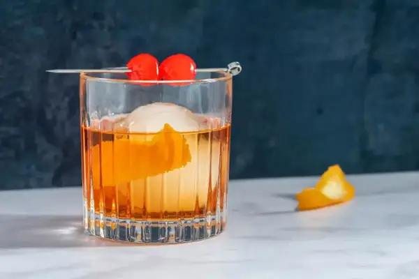 Klasyczny koktajl Old Fashioned z pomarańczą i wisienkami na patyczku.