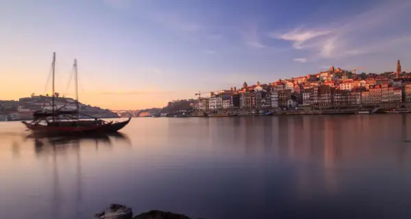 Barcos tradicionales navegan por el río Duero al amanecer, con la pintoresca ciudad de Oporto al fondo. Un lugar imprescindible que ver en el norte de Portugal.