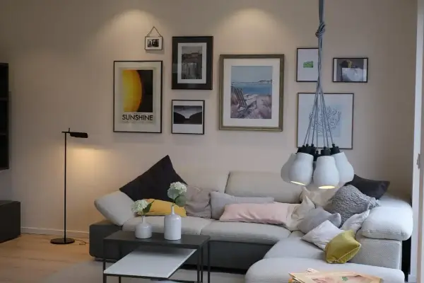 Przytulne mieszkania w Danii: salon z wygodną kanapą, galerią ścienną i designerską lampą.