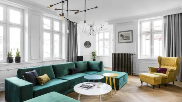 Zielona kanapa w salonie inspiracje: nowoczesny salon z dużą, welurową kanapą w kolorze butelkowej zieleni, żółtym fotelem i okrągłymi stolikami.